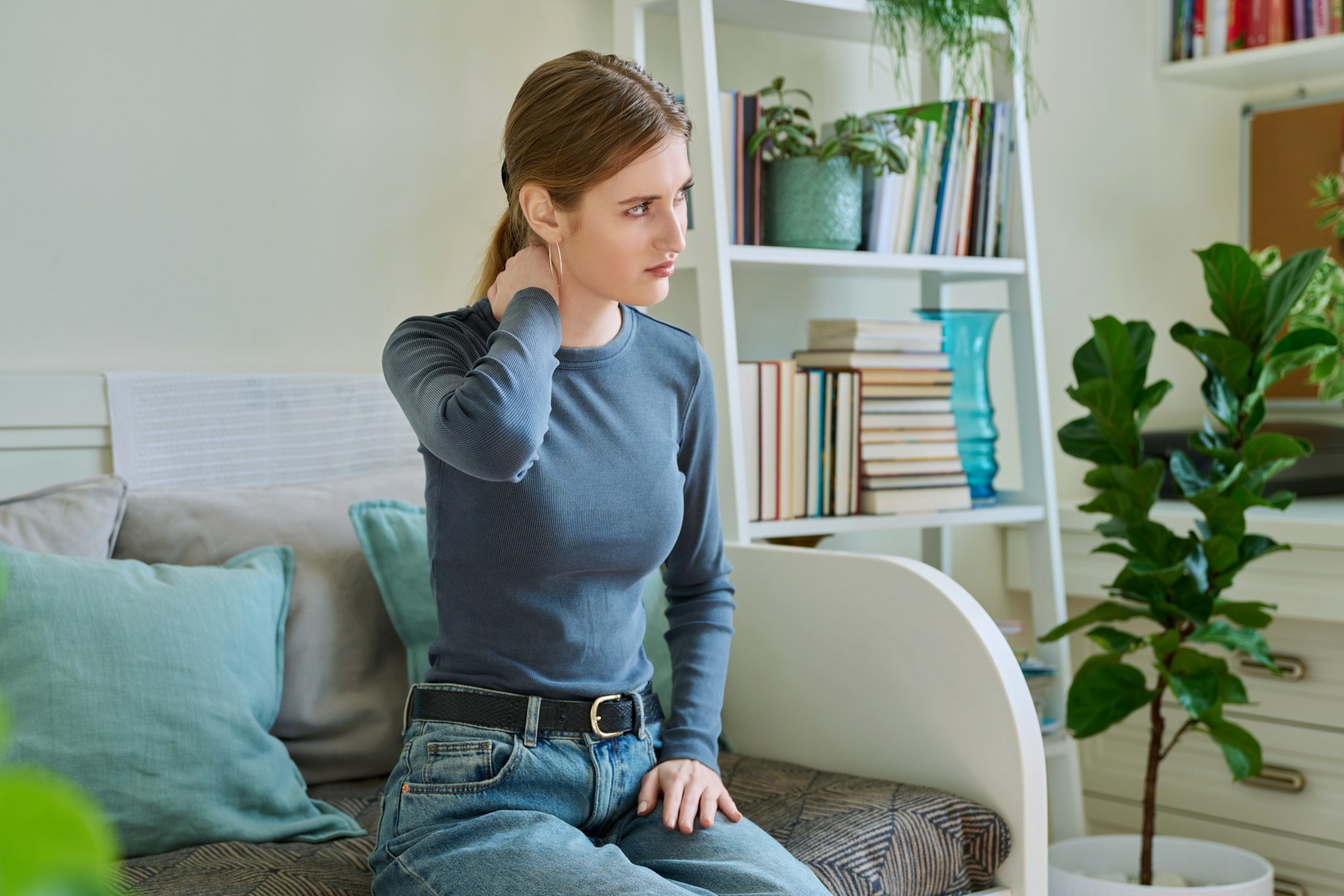 Young teenage female experiencing neck pain sitting on couch at home